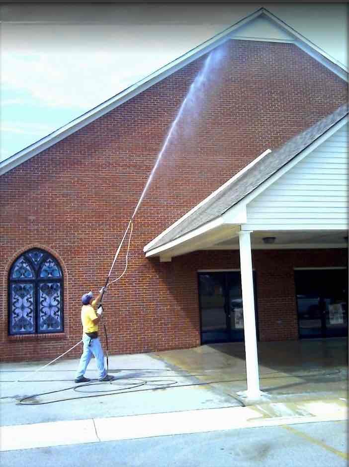 Man pressure washing a commercial brick building with a long wand